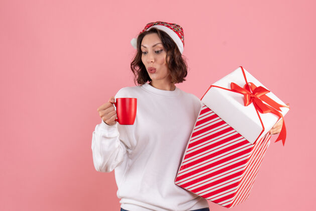 圣诞节年轻女子手持圣诞礼物和粉红色墙上的一杯茶的前视图微笑人杯子