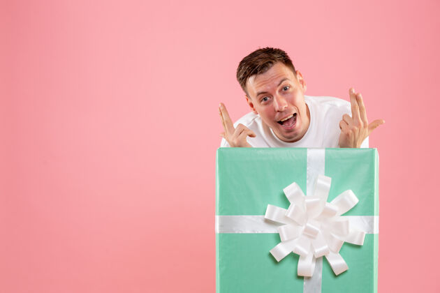 盒子一个年轻人躲在粉红色的墙上礼物的正面视图快乐情感隐藏