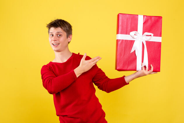 成人黄色墙上拿着圣诞礼物的年轻人的正视图庆祝男性礼物