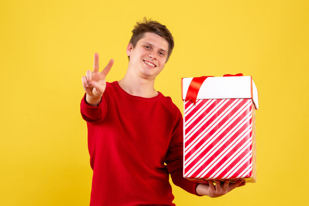 圣诞快乐手持圣诞礼物的年轻人在黄色墙壁上微笑的正面视图情感礼物快乐