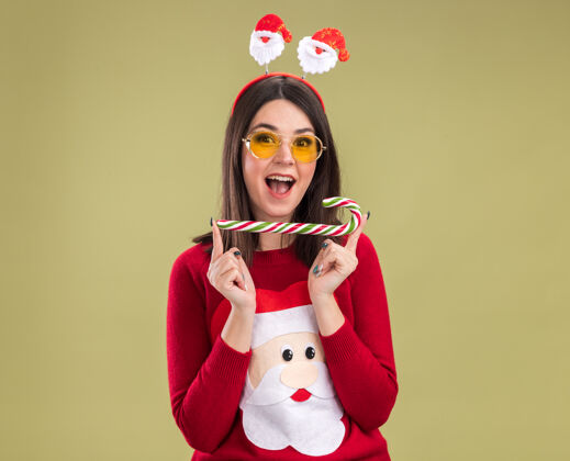 女孩令人印象深刻的年轻漂亮的白人女孩穿着圣诞老人毛衣和头带眼镜举行传统的圣诞糖果手杖水平横向新年手杖