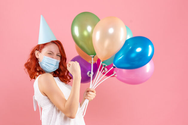 庆祝粉红色墙上戴着无菌面具的年轻女子的正面照片多彩气球派对