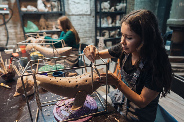 雕刻在工作室里享受最喜爱工作的年轻女子的肖像波特小心地在泥鲸上工作艺术工作室艺术家室内