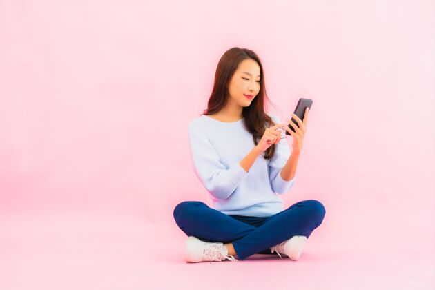智能手机肖像美丽的亚洲年轻女子在粉色隔离墙上使用智能手机女学生彩色休闲