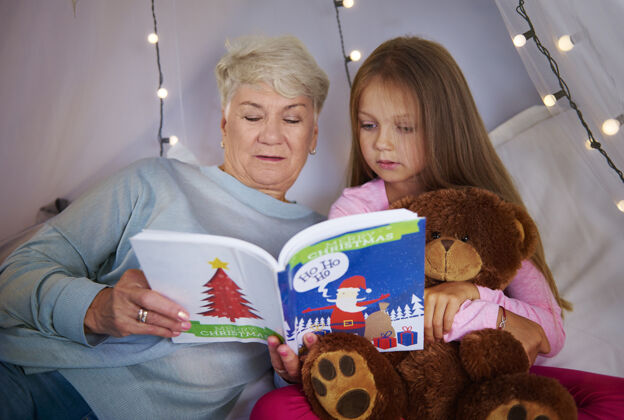 圣诞节孙女和奶奶在看图画书结合坐着老年人