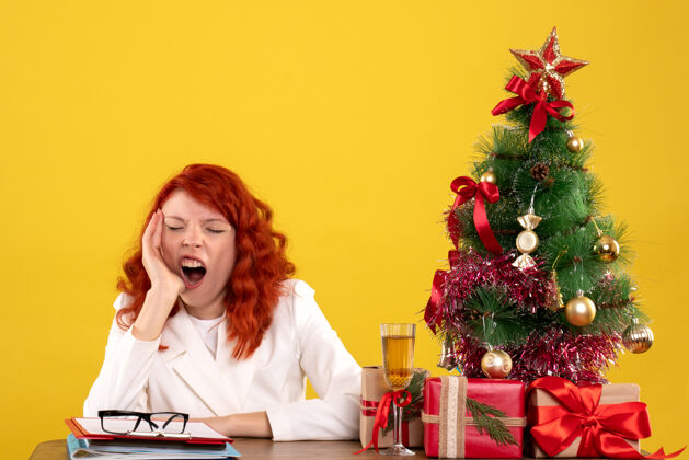 圣诞节女工人坐在桌子后面 手里拿着圣诞礼物和黄色的圣诞树女桌子成人