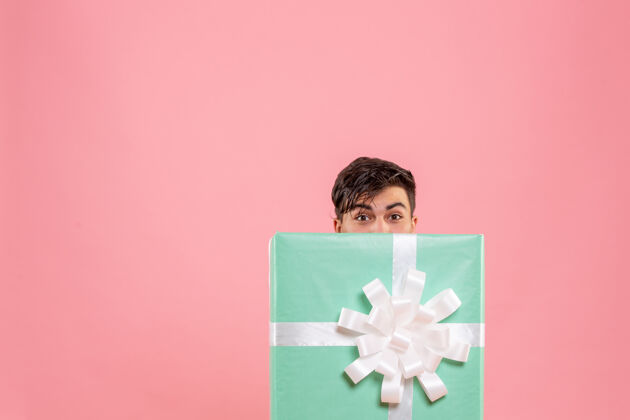 隐藏一个年轻人躲在粉红色的墙上礼物的正面视图礼品盒里面前面