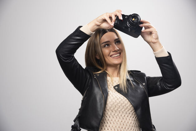 女性穿皮夹克的女孩在照相机上查看她的照片记录数码成人女人