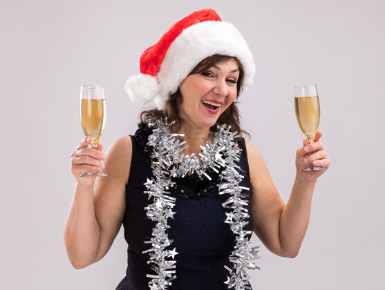 脖子快乐的中年妇女戴着圣诞帽 脖子上戴着金箔花环 手里拿着两杯香槟 看着隔离在白色背景上的相机中年花环帽子