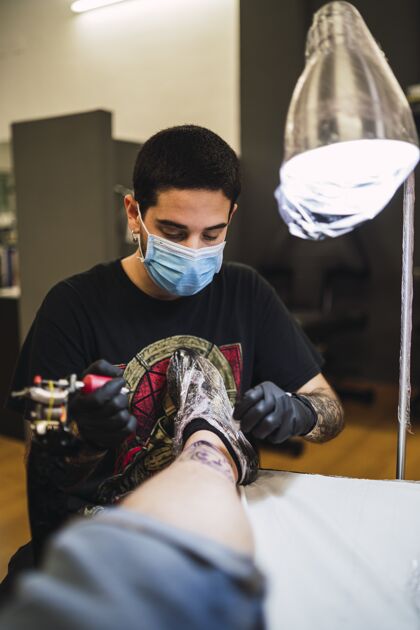 风格一位男性纹身艺术家在客户腿上纹身的照片家伙手套机器