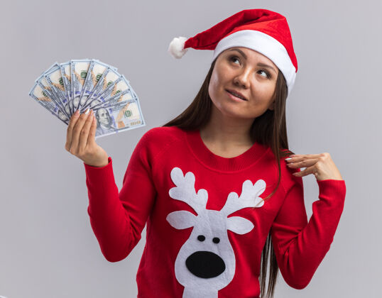毛衣令人印象深刻的仰视年轻的亚洲女孩戴着圣诞帽和毛衣拿着现金把手放在肩膀上隔离在白色背景上现金肩放