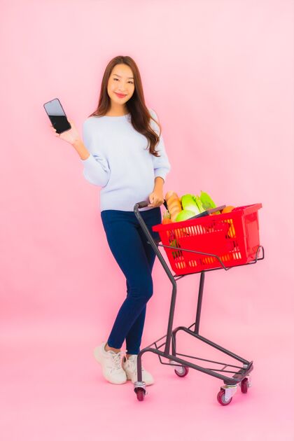 饮食一幅美丽的亚洲年轻女子的画像 粉红色的隔离墙上 篮子里放着水果蔬菜和杂货女人购买泰国
