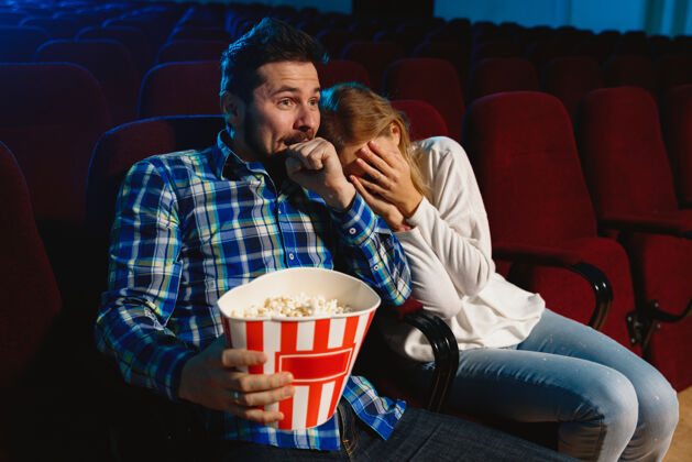 年轻迷人的年轻白种人夫妇在电影院 房子或电影院看电影看起来富于表现力 惊讶和情绪化独自坐着玩关系 爱情 家庭 周末时间二舒适男性