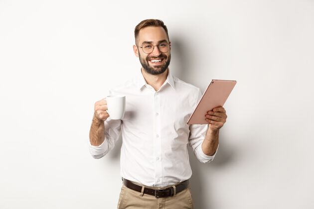 胡须满意的老板喝茶和使用数字平板电脑 看书或工作 站着企业家科技成人