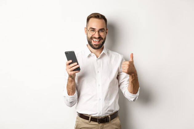 设备满意的商人在使用手机后竖起大拇指 站着很高兴在线同意智能手机