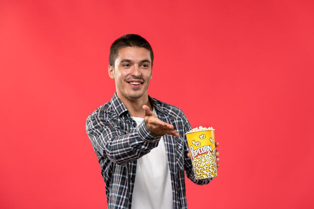 男人正面图年轻男子手持爆米花包在浅红墙电影院看电影男电影电影肖像年轻男性