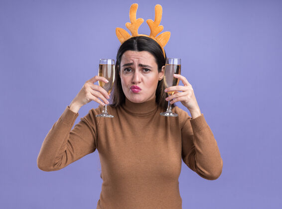 毛衣撅起嘴唇年轻漂亮的女孩穿着棕色毛衣 戴着圣诞发箍 耳朵周围拿着两杯香槟 背景是蓝色的耳朵头发嘴唇