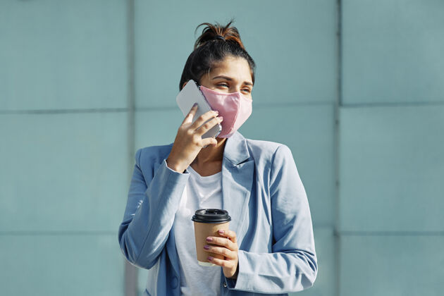 医疗口罩大流行期间 戴着医用口罩和咖啡的女人在机场用智能手机交谈航程Ncov机场