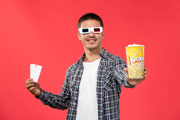 帅哥正面图年轻男子手持爆米花和票在红墙电影院的d太阳镜票西装年轻男性