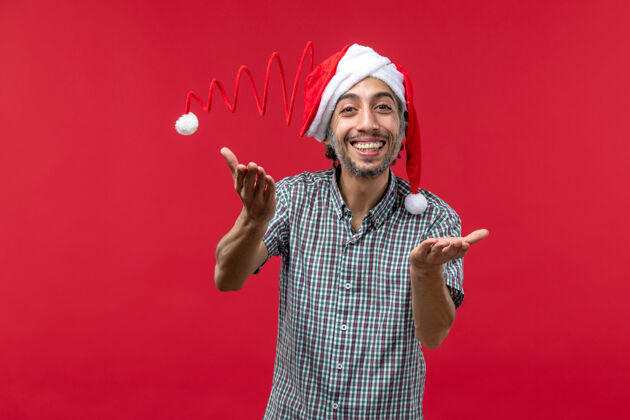快乐红墙上戴着圣诞玩具帽的年轻人的正视图漂亮男性节日