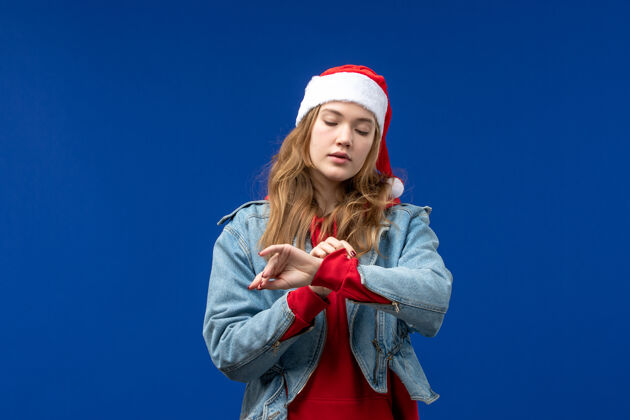 年轻女性前视图年轻女性在蓝色背景上检查时间圣诞节情感色彩冬天人服装