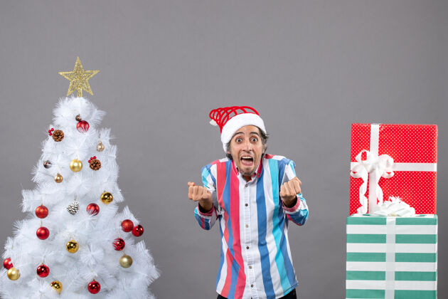 人站在白色圣诞树旁的震惊男人的前视图站立震惊圣诞