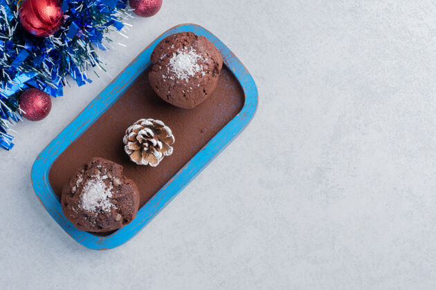 糖巧克力纸杯蛋糕和松果放在盘子旁边的花环和大理石表面的圣诞饰品纸杯蛋糕蛋卷零食