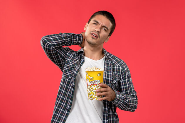 男性正面图：年轻男子拿着爆米花包 在红面电影院里脖子疼电影年轻男人