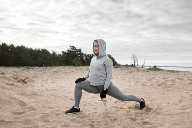 女孩户外图片有吸引力的苗条肌肉年轻的女运动员穿着时髦的运动服在沙滩上锻炼 做弓箭步 跑步前热身运动 健身 柔韧性和力量户外姿势年轻