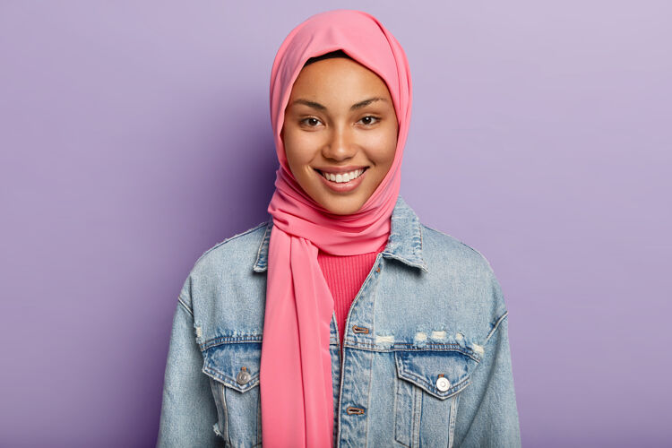传统庆幸东方女性信奉伊斯兰教 头上蒙着粉色面纱 微笑温柔 露出洁白的牙齿 隔离在紫罗兰色的墙壁上表达积极的情感和情感种族室内女人阿拉伯