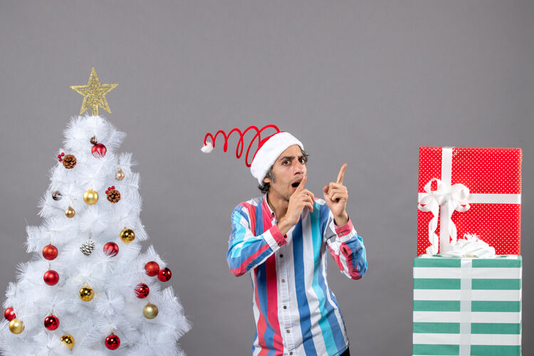 人正面图：体贴的男人用手指指着站在白色圣诞树旁的东西男点圣诞节
