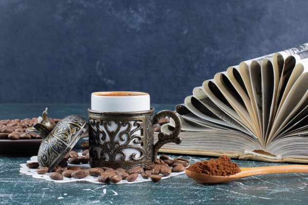 一杯泡沫咖啡 一盘咖啡豆和一本大理石桌上的书咖啡磨碎的杯子