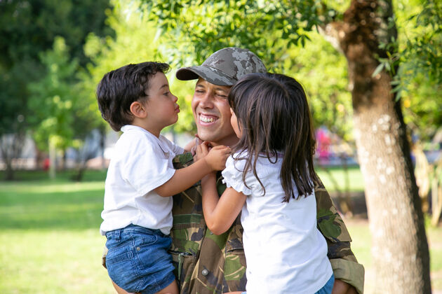 朋友高加索男人抱着孩子 微笑着快乐可爱的孩子们拥抱亲吻着身着军装的中年父亲爸爸从部队回来家庭团聚 做父亲 回家的概念户外儿子女儿