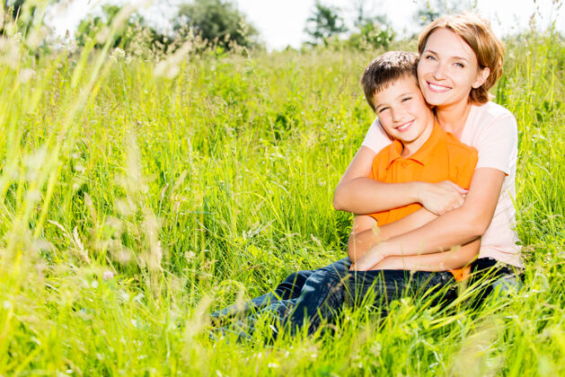 拥抱快乐的母子在春天的草地户外写真玩耍母性儿子