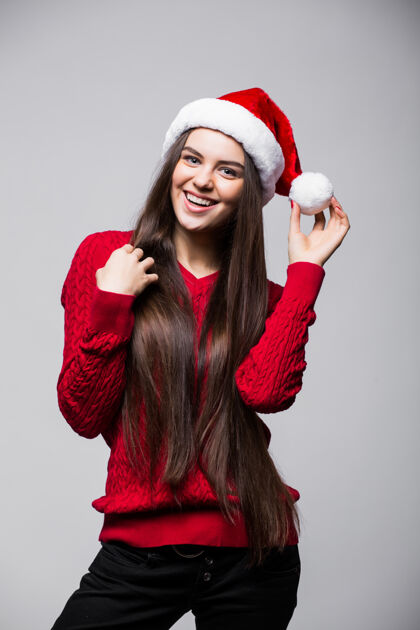 圣诞老人微笑着戴着圣诞老人帽子的可爱的年轻女子站在灰色的墙上 抬头仰望圣诞老人微笑成年人