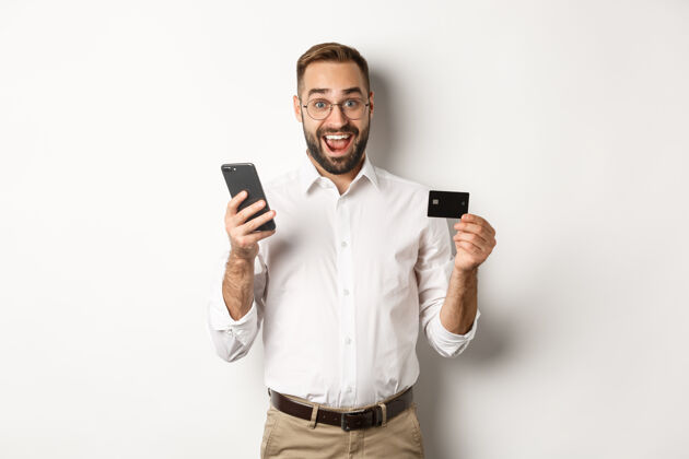 信用商务和在线支付兴奋的男人用手机和信用卡支付 微笑着惊讶 站着员工智能手机买家