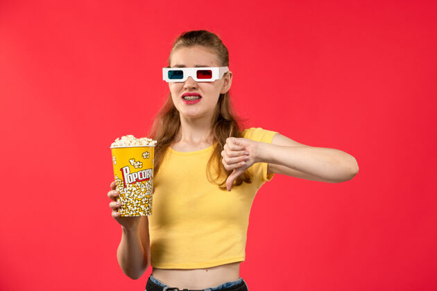 风景前视图年轻的女性在电影院举行爆米花包在d太阳镜上的红墙电影爆米花年轻的女的电影