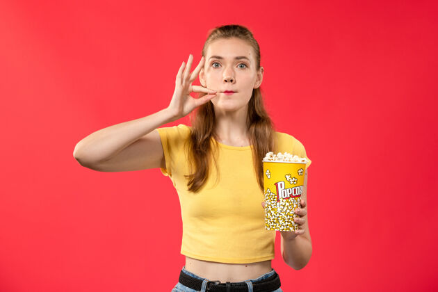 成人前视图年轻的女性在电影院拿着爆米花包在浅红色的墙上电影院年轻女性女性爆米花