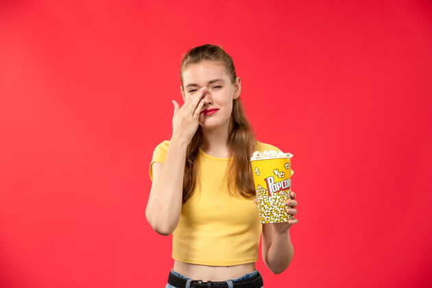 电影正面图年轻的女性在电影院拿着爆米花在红墙电影院的女性色彩爆米花剧院视图