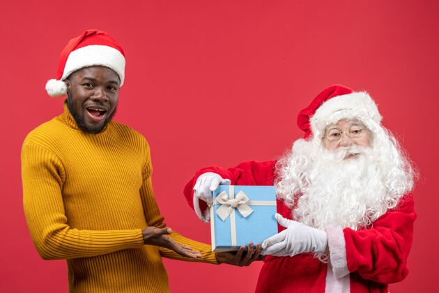 冬天红墙上的圣诞老人和拿着礼物的年轻人的正视图快乐服装节日