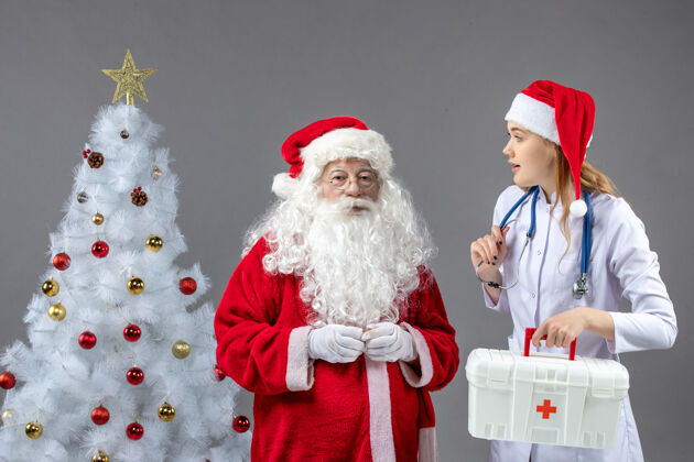 快乐圣诞老人和年轻女医生在灰色墙壁上的正视图节日圣诞老人十二月