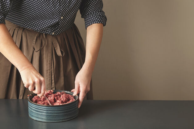 磨碎不可辨认的女人用钢勺子把肉末和香料混合在陶瓷蓝色的碗里 放在老式桌子的一边美国配料猪肉