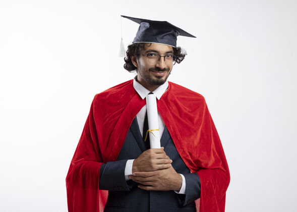 西装年轻的白种人超级英雄 戴着眼镜 穿着红色斗篷的西装 戴着毕业帽 手里拿着一张隔离在白色背景上的毕业证书 上面留有复印空间眼镜斗篷白色