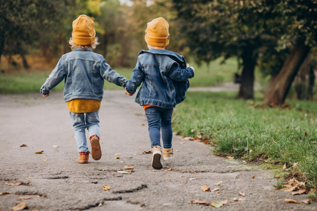 黄色帽子两个男孩兄弟在秋天的公园里跑步友谊卷发朋友