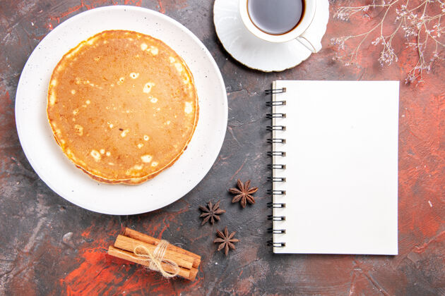 混合自制煎饼的垂直视图肉桂石灰一杯茶和笔记本放在五颜六色的桌子上热的酸橙笔记本