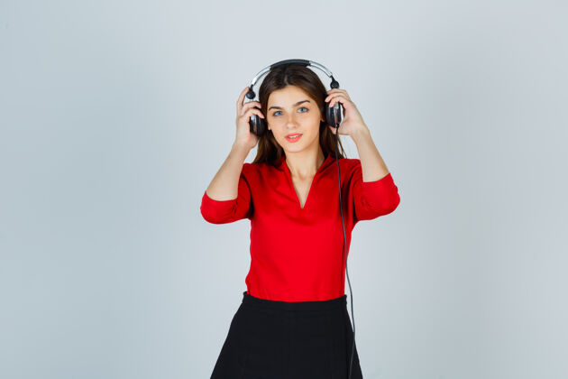 成人戴着耳机的年轻女士站在红衬衫里摆姿势裙子迷人人