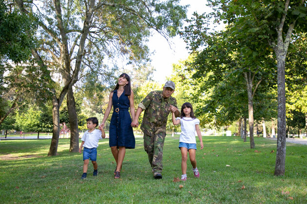 男人一家人在公园的草地上散步 父亲穿着军装给女儿看东西 长发的母亲微笑着 家庭团聚 回家的概念长发帽子妈妈