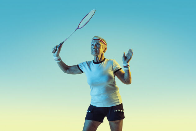 装备高级女子在霓虹灯下穿着运动服在斜坡上打羽毛球快乐球员姿势