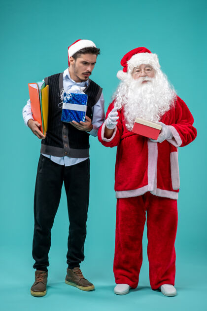庆祝圣诞老人与年轻男性和礼物在蓝色墙上的正面视图圣诞快乐假期假日