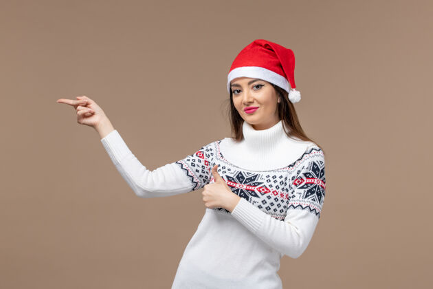 帽子正面图棕色背景上戴着红色圣诞帽的年轻女性感慨圣诞新年微笑模特快乐